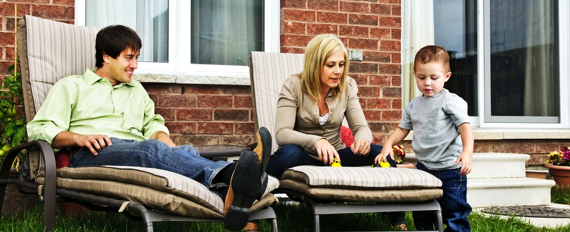 Happy family relaxing in backyard of new home with toddler